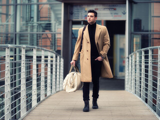 Confident young man walking in fashionable trench coat through city street.
