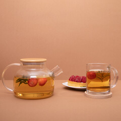 Fruit tea with citrus, berries, and rosemary in a glass teapot, served with raspberry dessert and a cup on a beige background. Fruit tea. Seasonal drink concept. Mock-up template