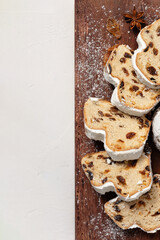 Pieces of stollen, sliced on wooden board, on beige table background, copy space, flat lay. Traditional bread with raisins and sugar powder, holiday winter bakery