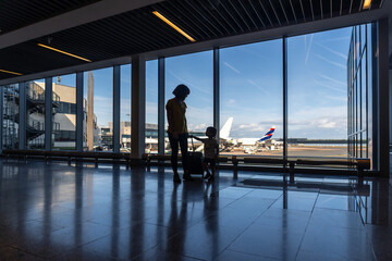 Silhouette of mother and son with luggage near the window in the airport looking at planes before...