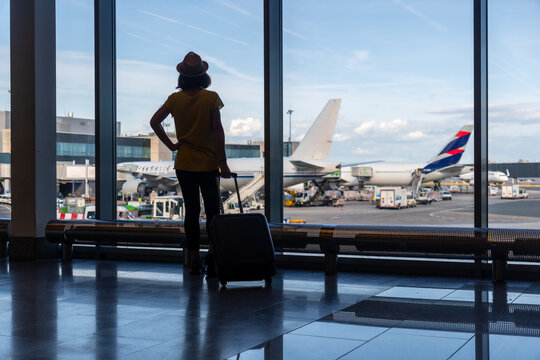 Silhouette of woman with a suitcase in the airport terminal looking at the planes waiting for the flight