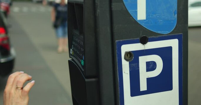Closeup elegant female hand type license plate number on parking meter keypad. Unrecognizable woman buy parking ticket on outdoors parking lot on sunny summer day.