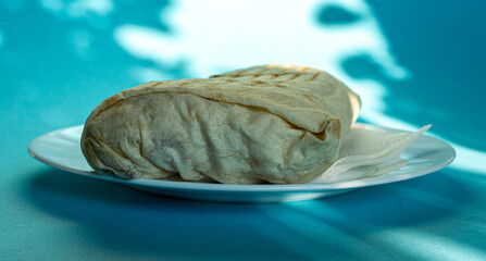 Large shawarma on a white plate with a napkin on a blue background with shadows. Food, healthy fast food, delicious to eat.