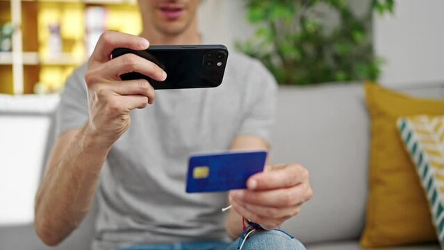Young hispanic man make photo to credit card by smartphone at home