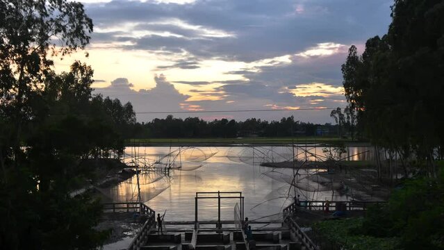 Beautiful sunset timelapse of a river in Bangladesh. The sun dips below the horizon, casting a golden glow over the village. The sky is ablaze with color, from fiery reds and oranges to soft pinks.
