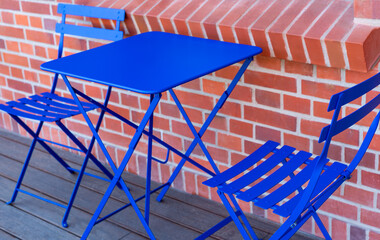 A purple colored metal patio table near a restaurant in front of the brick wall.