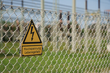 Yellow High Voltage, Danger Sign Attached To Chain Link Fence And Electric Power Plant In...