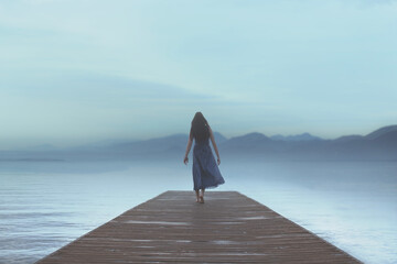 woman walking alone on a pier by the sea in a surreal atmosphere in the blue hour