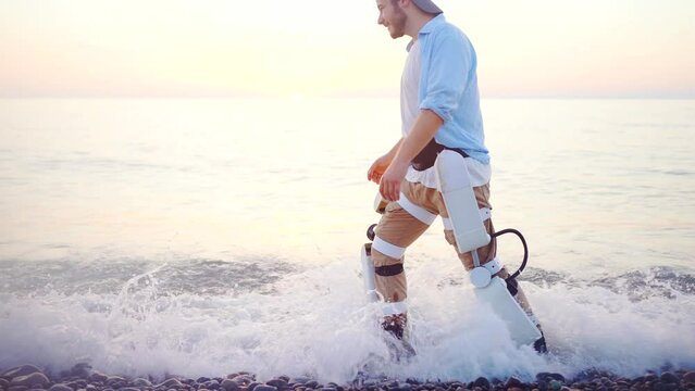 a happy man in an exoskeleton suit walks along the beach at sunset