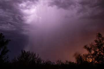 A rain shaft at sunset is illuminated by lightning in the desert
