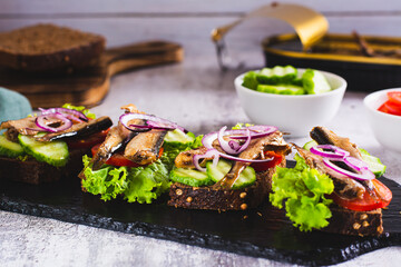 Sandwiches on rye bread with tomatoes, cucumber, sprats and onions on slate