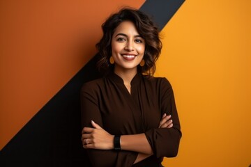 Portrait of a happy young woman standing with arms crossed over orange and black background