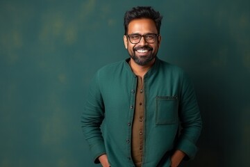 Portrait of a smiling indian man wearing glasses standing against green wall