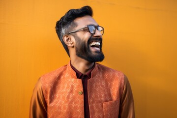 Portrait of a happy young indian man laughing against yellow background