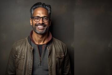 Portrait of a happy Indian man with glasses against black background.