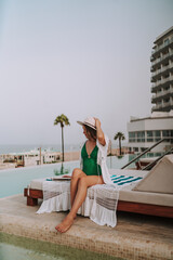 Chica joven en hamaca con smartphone tomando fotograf&iacute;as y leyendo en piscina de hotel de lujo