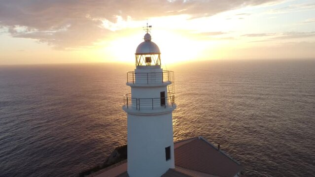 Drone footage over Far de Capdepera lighthouse tower with golden sunset sky in Spain