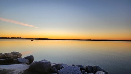 Scenic view of rocks covered with snow against a tranquil lake at sunset