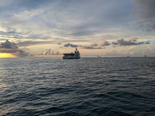 Large ship sailing peacefully through the open waters of the sea at sunset with wispy clouds