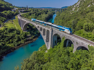 An aerial view of a train crossing the stone railway bridge on the outskirts of the town of Solkan...