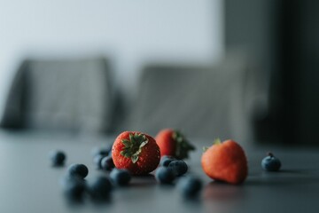 strawberries and blueberries sit on a table near one another
