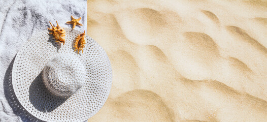 Top view of a beach hat with seashells on the sand under the hot summer sun, horizontal banner. Concept of sandy beach holiday, flat lay, background with copy space for text