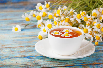 Daisy flowers in a white cup of tea, chamomile herbs on wooden background. Herbal medicine. Healthy lifestyle concept.