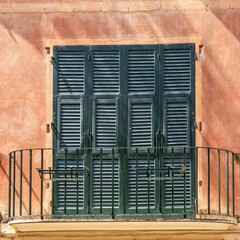 Terrace featuring dark green window shutters on an orange-colored building.