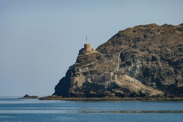 Fototapeta na wymiar Majestic castle stands atop a hill overlooking the beautiful coastline of Oman in the Middle East