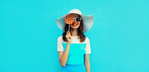 Portrait of happy young woman with colorful lollipop wearing summer straw hat, sunglasses, dress on...