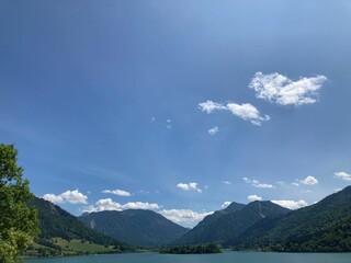 Obraz premium Scenic view of a tranquil lake surrounded by lush green trees and a bright blue sky