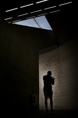 Silhouette of a man standing in a dimly lit underground room, illuminated by a single skylight
