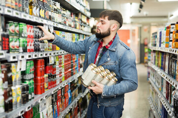 Young bearded guy shopping for drinks in supermarket, taking canned beer from shelves .