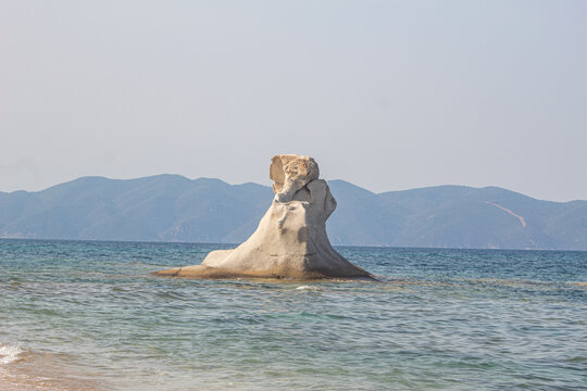 Rock shaped like elephant on beach in Greece surrounded by ocean. Interesting natural rock structure. Visible mountains in the baackground