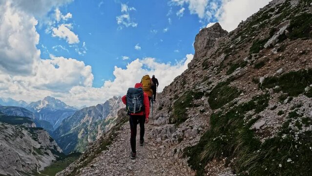 Active people with backpacks hiking narrow pathway and climbing Tre Cime di Lavaredo Dolomites mountain. Group of friends summer adventure journey in nature. Travel exploring Alps, Dolomites, Italy