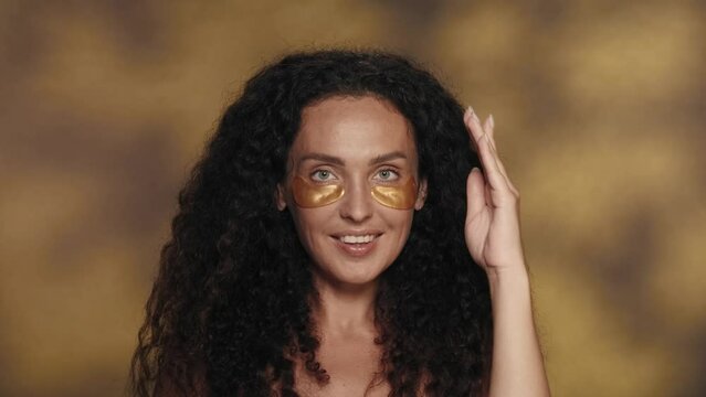 The woman opens her face, removing the palms that covered it. A woman with golden patches under her eyes sends an air kiss in the studio on a yellow background with highlights.