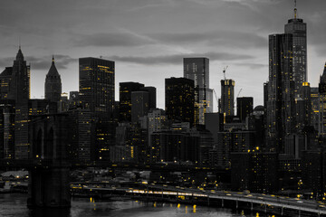 Yellow lights shining in black and white night time cityscape with the Brooklyn Bridge and...