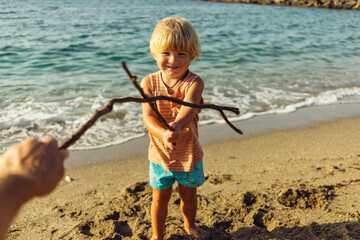 little boy fencing on sticks with dad on the seashore
