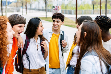 Diverse teenage student group having fun together talking at college campus. Millennial friends laughing and enjoying time outdoors.