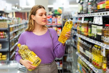 Pretty woman choosing vegetable oil for cooking during shopping in supermarket