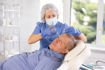 Obraz premium Female doctor conducting face revitalization procedure for old man patient by micro-injection method