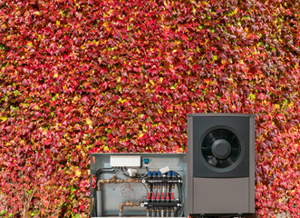 Herbst-Wärmepumpe und Heizkreisverteiler der Fußbodenheizung vor einer bepflanzten Hauswand