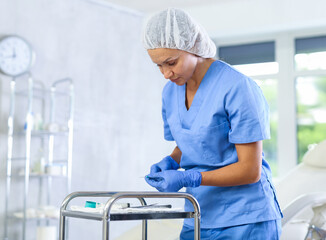 Focused female doctor standing near instrument tray in clinic office, preparing syringes for injection..