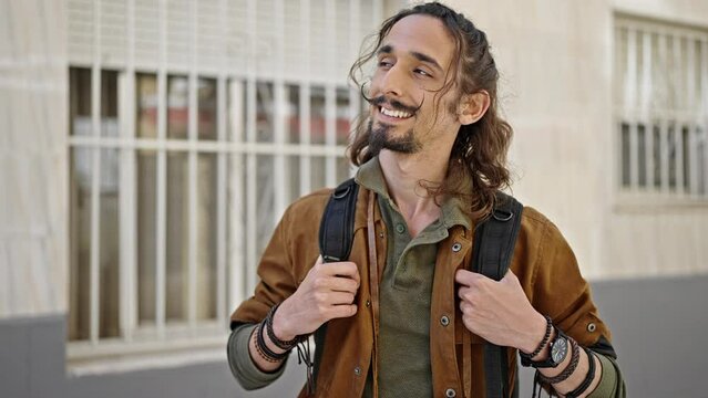 Young hispanic man tourist wearing backpack smiling at street