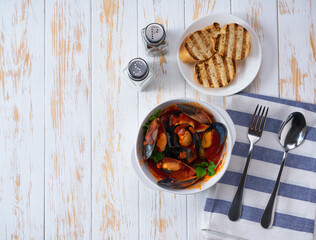 Traditional tomato soup with mussels with and toasted baguette on a white table, top view.