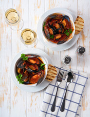 Two bowls with mussels soup with tomato sauce and toasted baguette on a white table, top view.