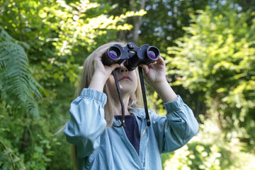 Cute little girl exploring nature looking through binoculars. Child playing outdoors. Kids travel,...