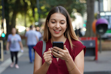 Close-up of young stylish woman using smartphone with ring holder to avoid thefts on the street in the metropolis with blurred people on the background