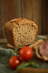 A sliced loaf of fresh homemade whole wheat bread. Tomatoes and ham are blurred in the foreground. Concept of healthy diet. Nutritious organic food. Aesthetic food presentation. Country style.