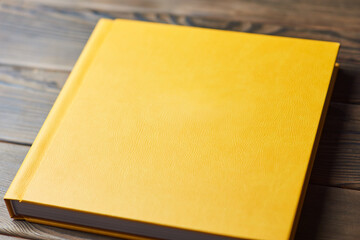 Stylish book with yellow leather hardcover isolated on a wooden background. Perspective view,...